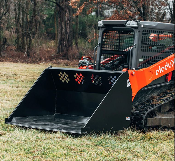 A bright orange compact track loader with a large black bucket attachment sits on a grassy field in front of trees.