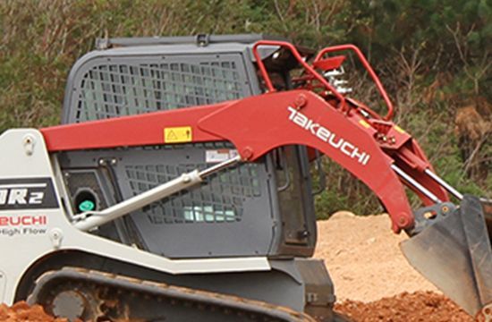 A Takeuchi tracked skid steer loader working on a dirt construction site.