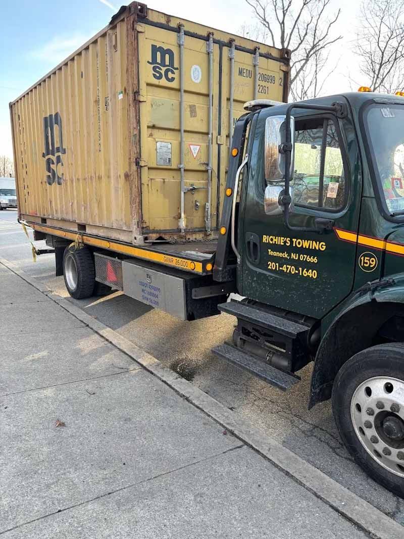 A tow truck is towing a shipping container down a street.