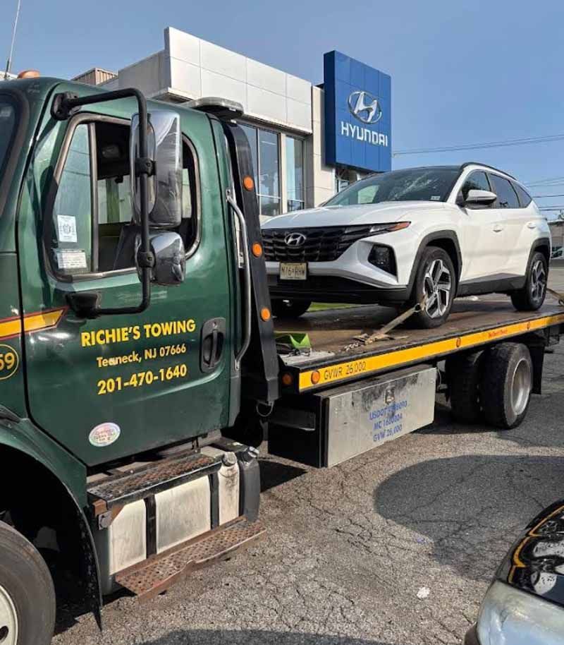 A tow truck with a white suv on the back is parked in front of a hyundai dealership.