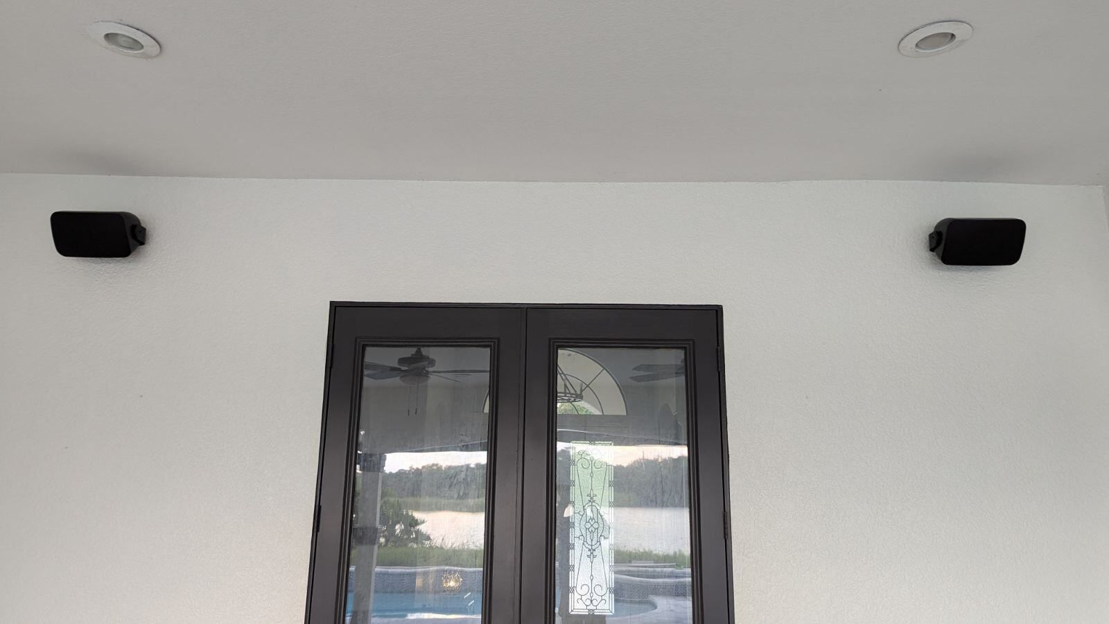 A pair of speakers mounted to the ceiling next to a window.