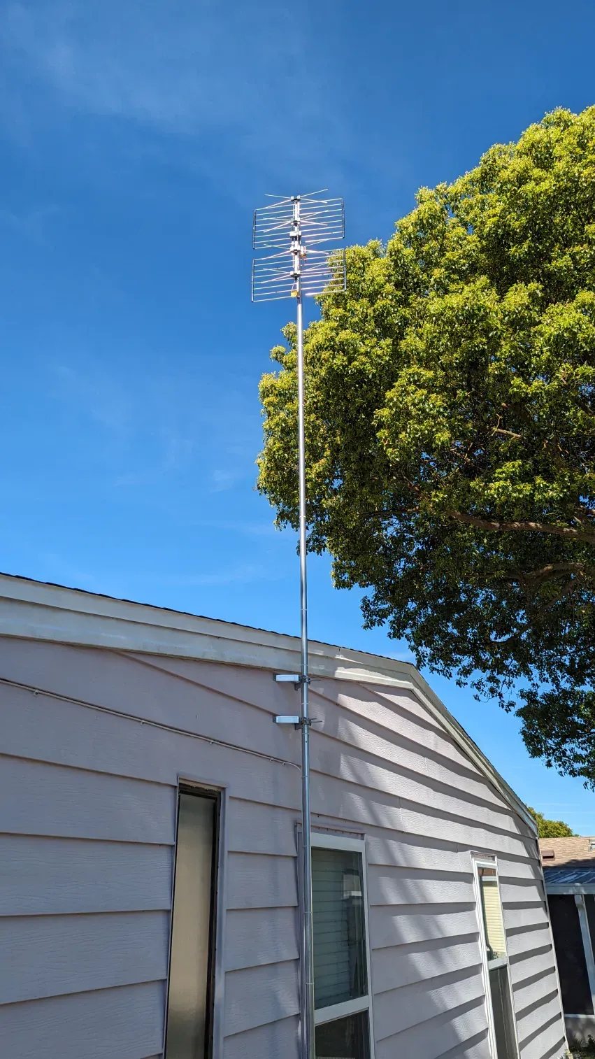 An antenna is sitting on the side of a house next to a tree.