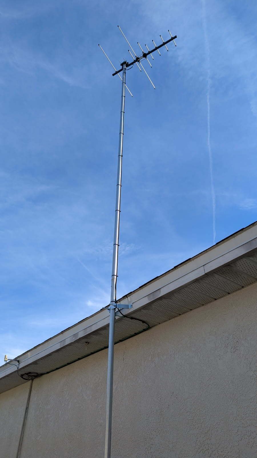 Television antenna mounted on a pole above a building's roof against a blue sky.