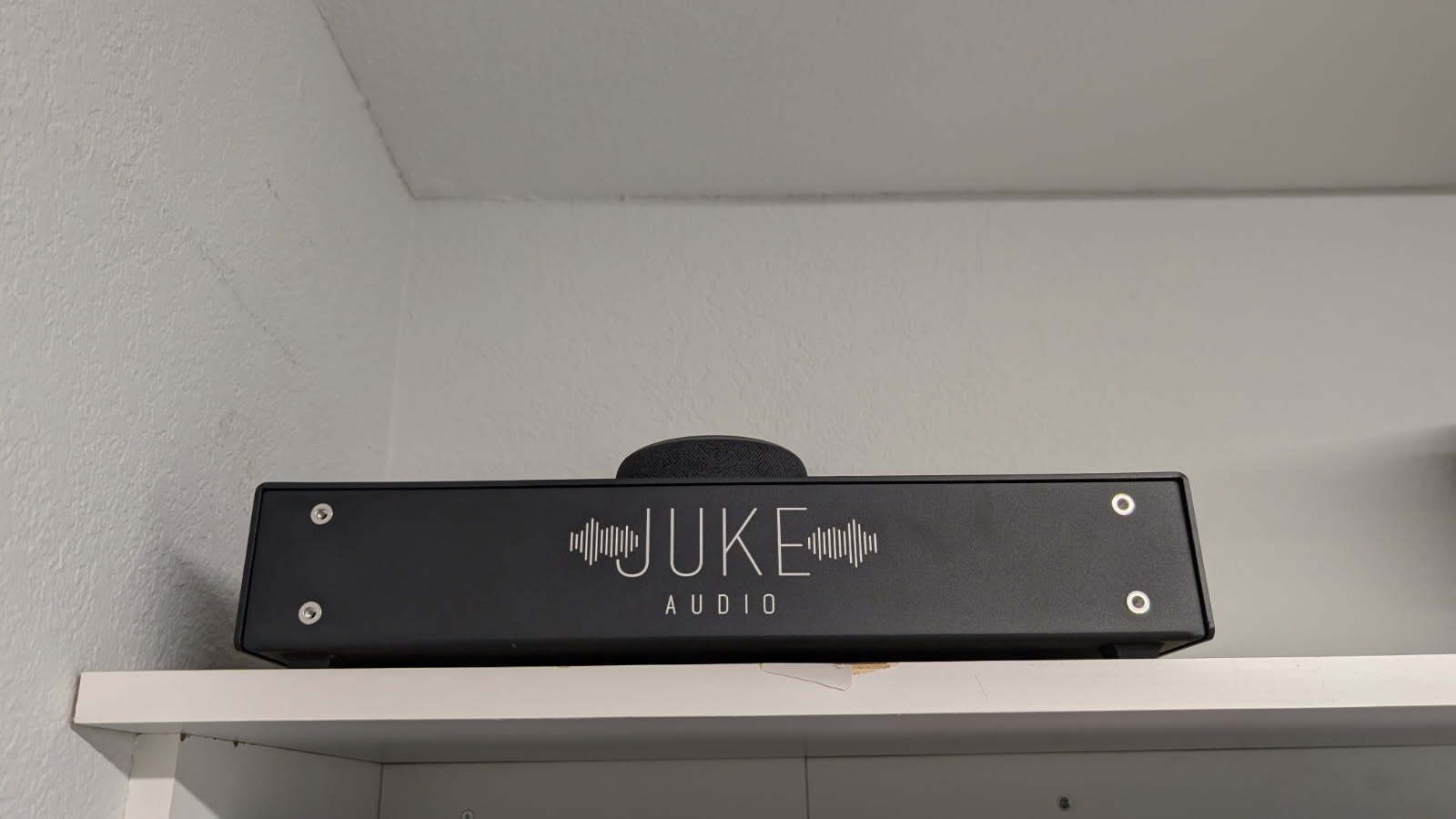 A black box with the word juke on it is sitting on a white shelf.