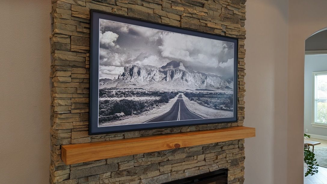 A black and white photo is hanging on a stone wall above a fireplace.