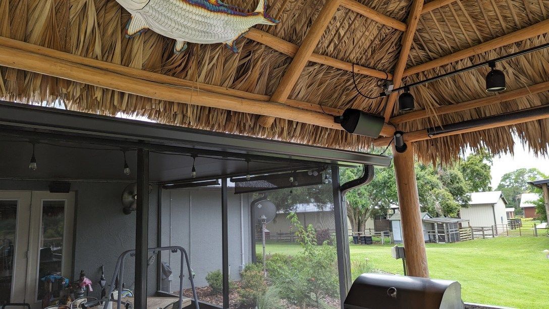 A patio with a thatched roof and a grill underneath it.