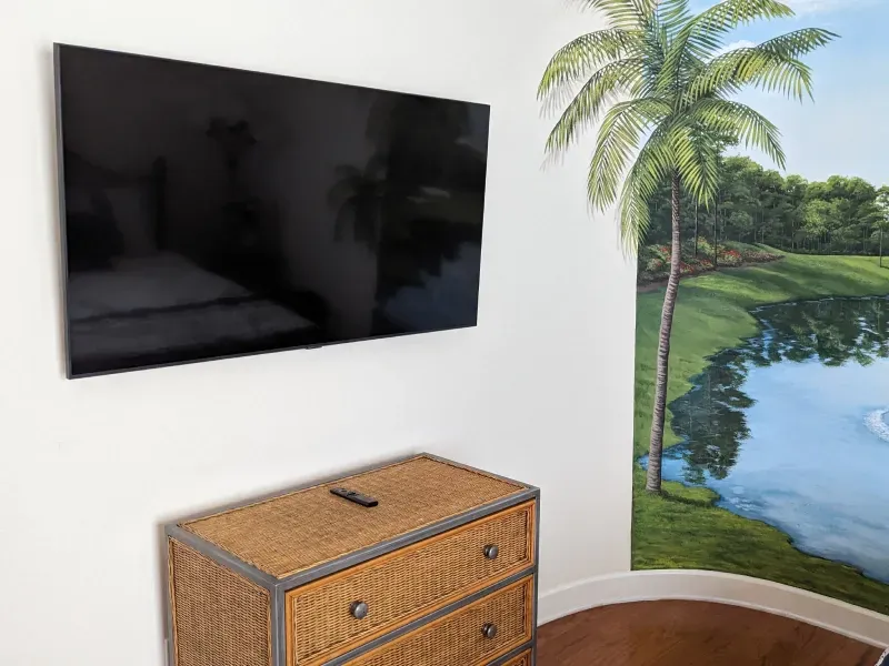 A bedroom with a dresser and a flat screen tv on the wall.