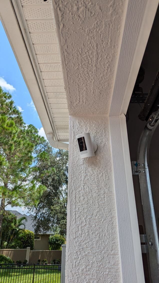 A security camera is mounted on the side of a white house.