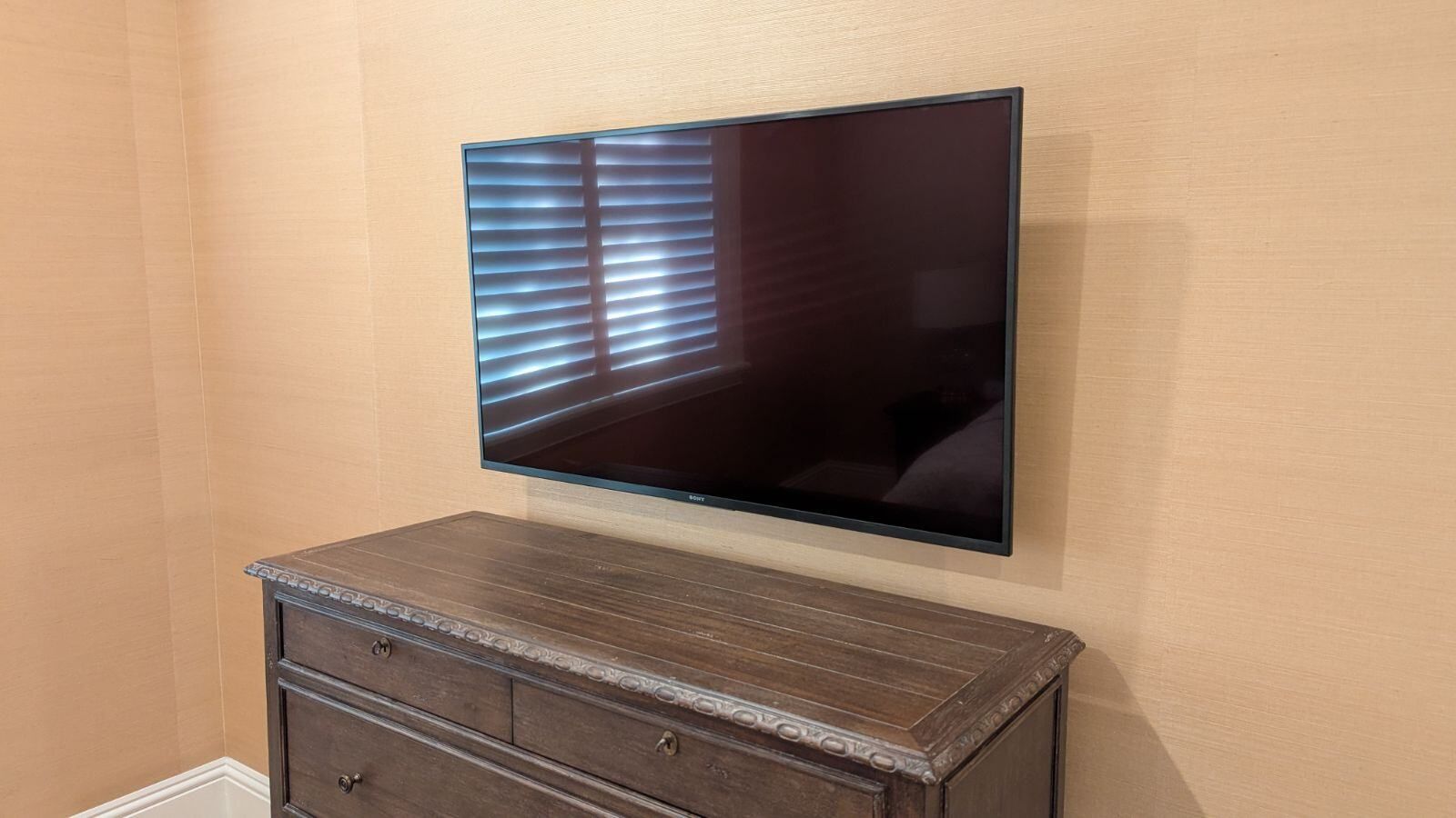 A flat screen tv is mounted on a wall above a dresser in a bedroom.