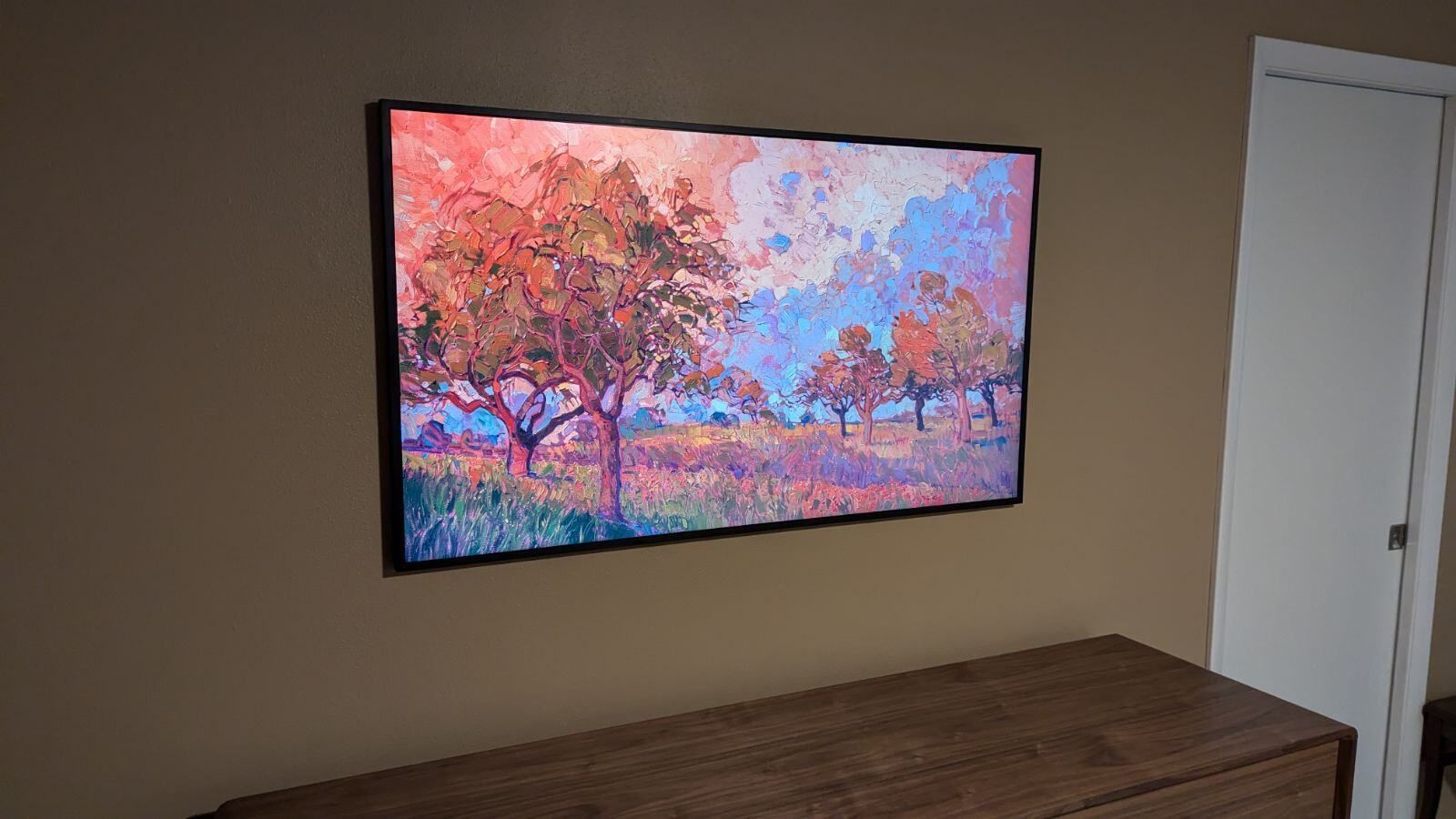 A flat screen tv is hanging on a wall above a wooden dresser.