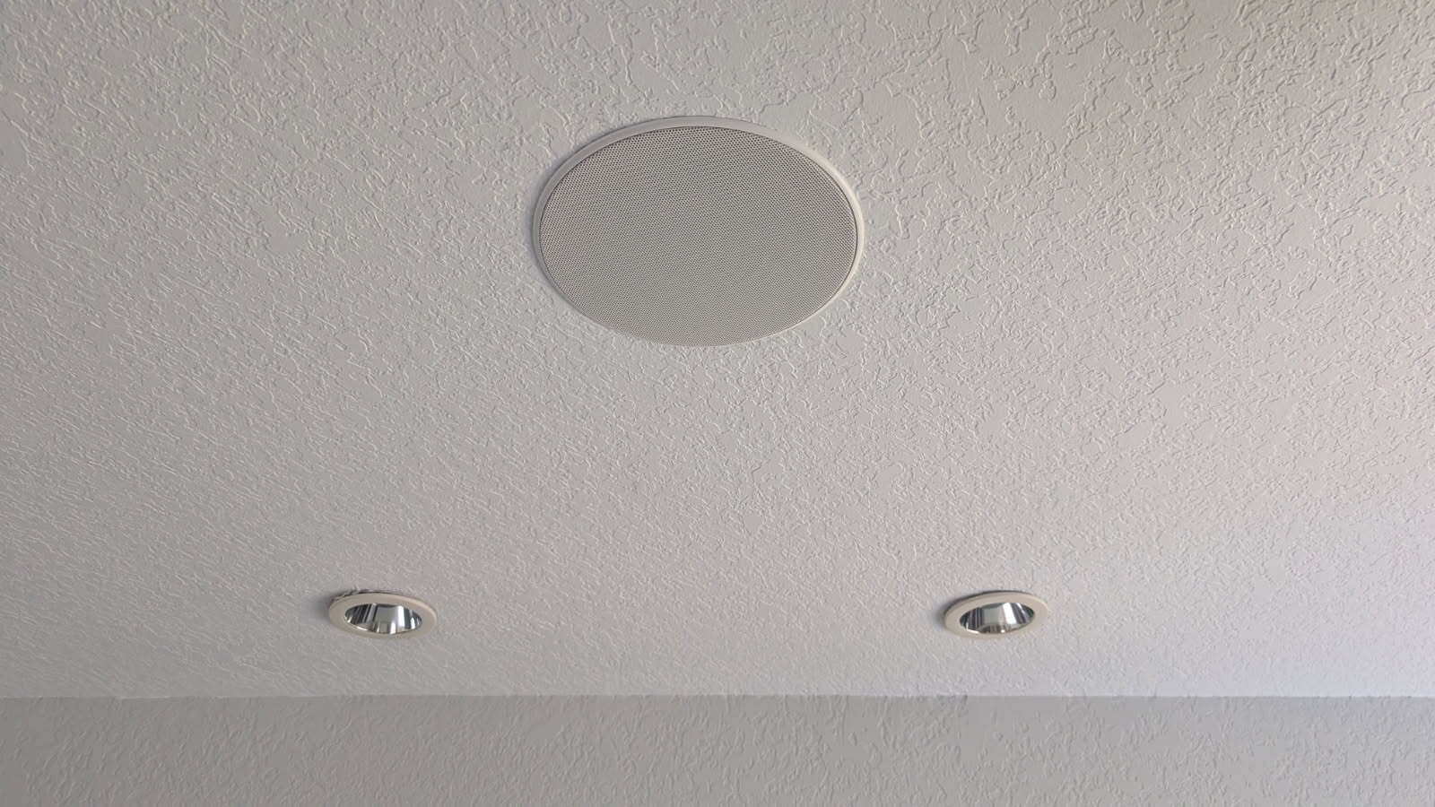 A round speaker is hanging from the ceiling of a room.