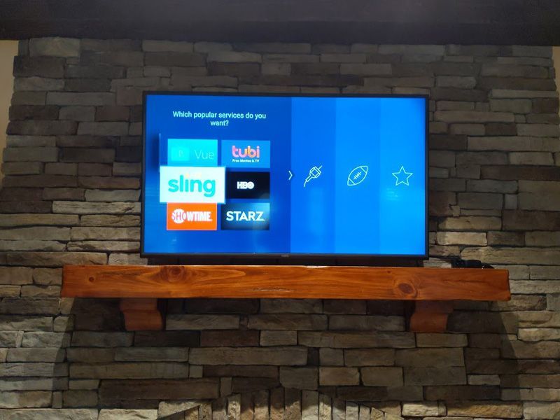 A flat screen tv is mounted on a wooden shelf in front of a stone wall
