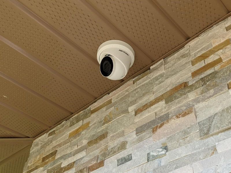 A security camera is mounted to the ceiling of a brick wall.