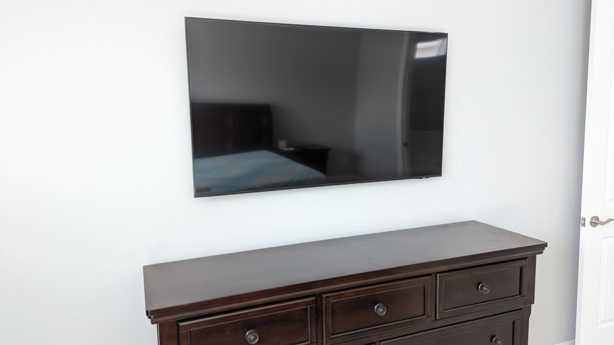 A bedroom with a dresser and a flat screen tv on the wall.