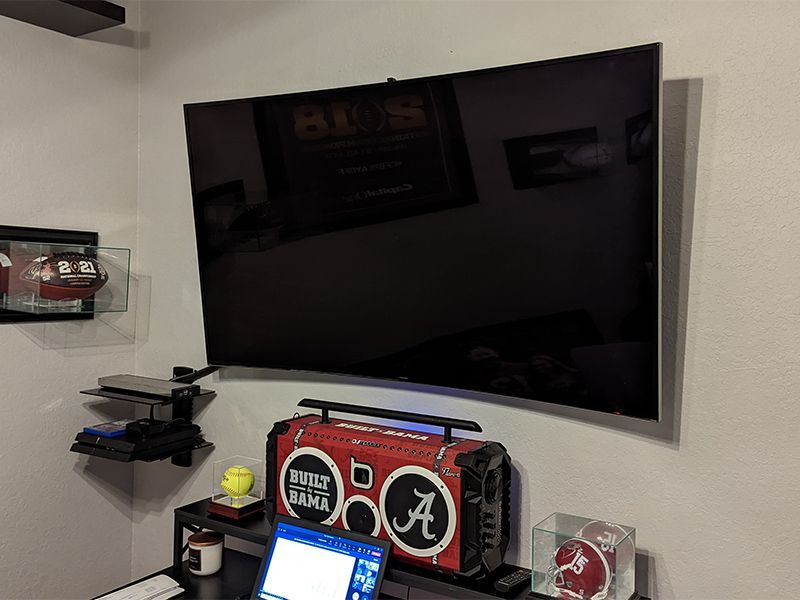 A large flat screen tv is mounted on a wall next to a laptop and a boombox.