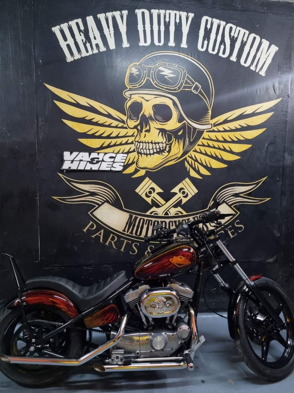 A motorcycle is parked in front of a sign that says heavy duty custom