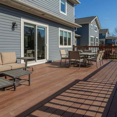 A wooden deck with a couch , table and chairs in front of a house.