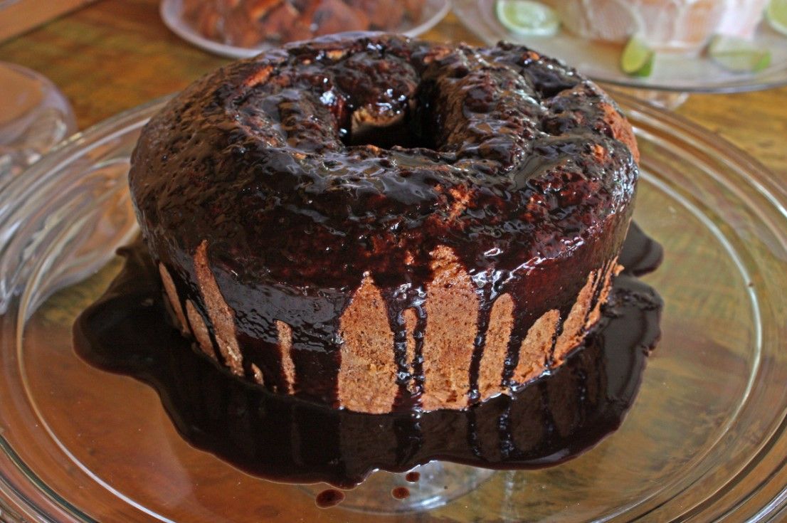 Um bolo de chocolate está em um prato de vidro sobre uma mesa.