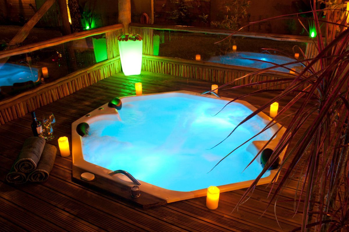 Uma banheira de hidromassagem cheia de água azul e velas em um deck de madeira.
