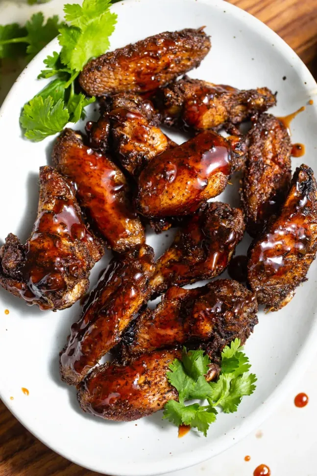 Crispy chicken wings with dark glaze on a white platter, garnished with cilantro.