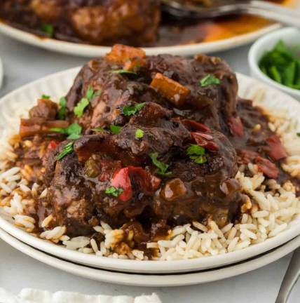 Oxtail stew with rice and vegetables on a white plate, garnished with parsley.