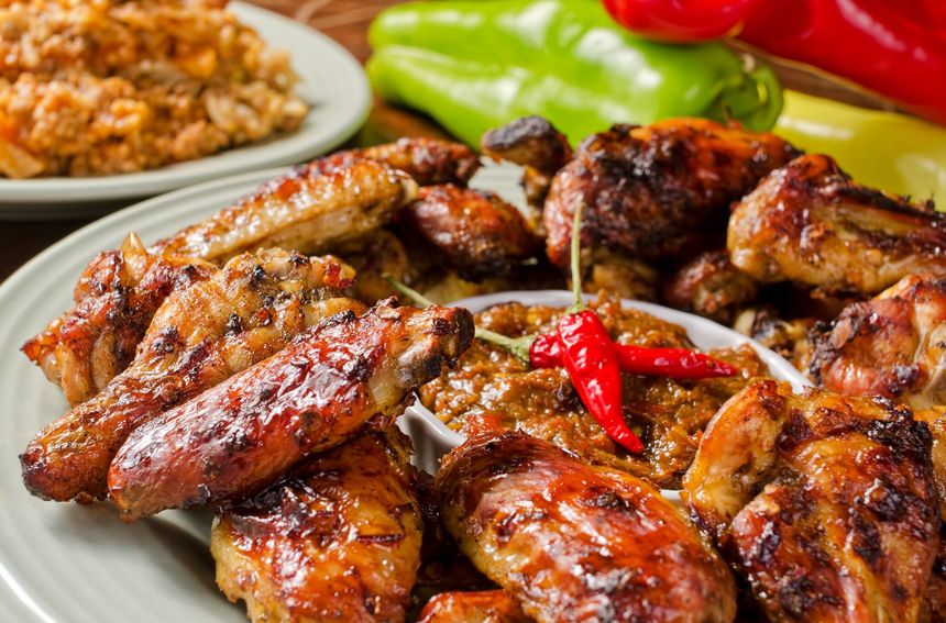 Grilled chicken wings and drumsticks with dipping sauce, peppers in the background.