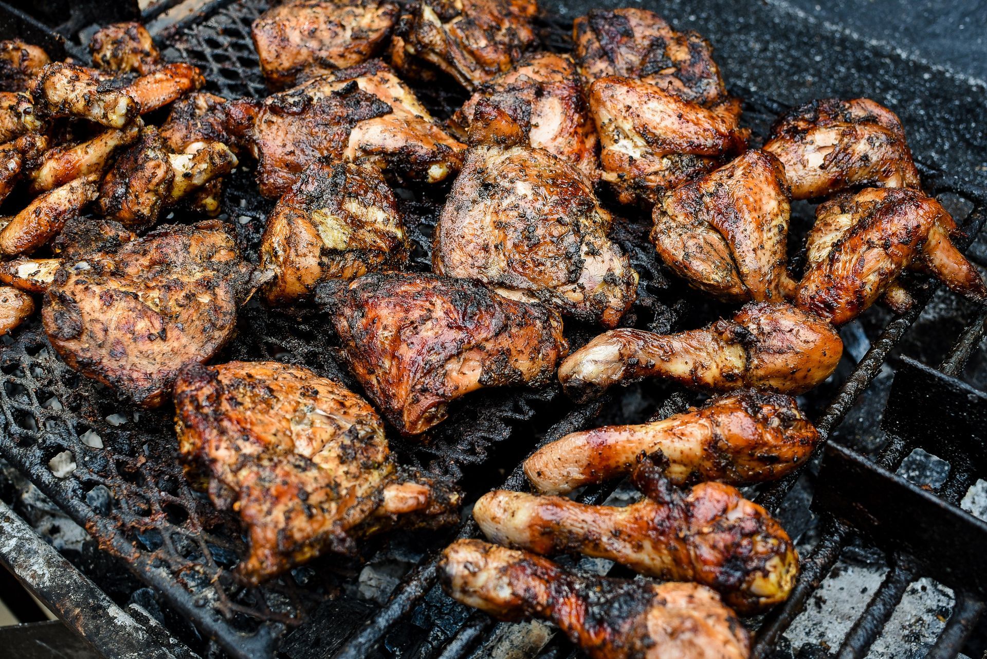 Grilled chicken pieces on a black grill; browned and charred from cooking.