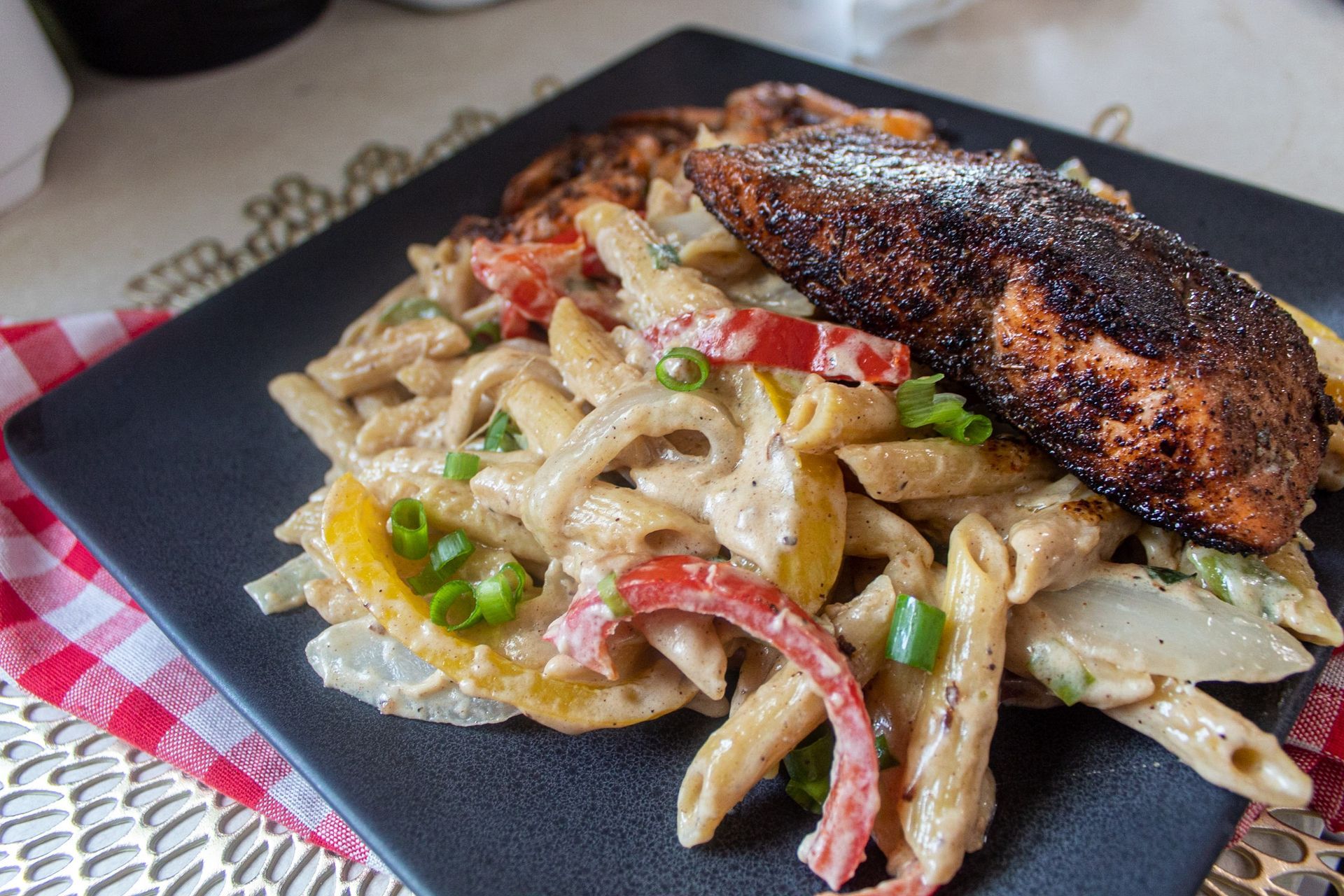 Blackened salmon and pasta with peppers, onions, and creamy sauce on a dark plate.