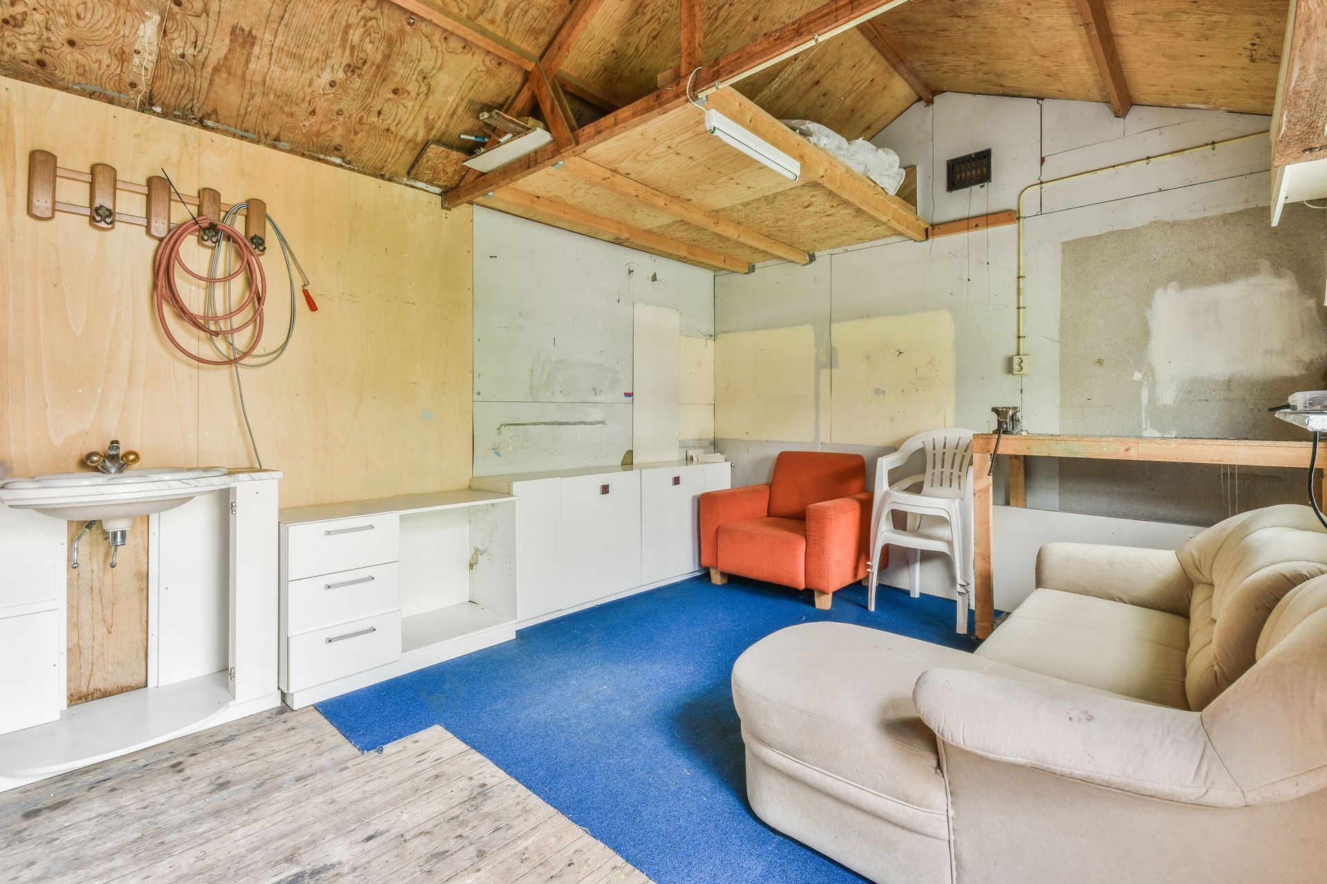 Garage interior with blue carpet, orange armchair, white sofa, work area, and wooden storage.
