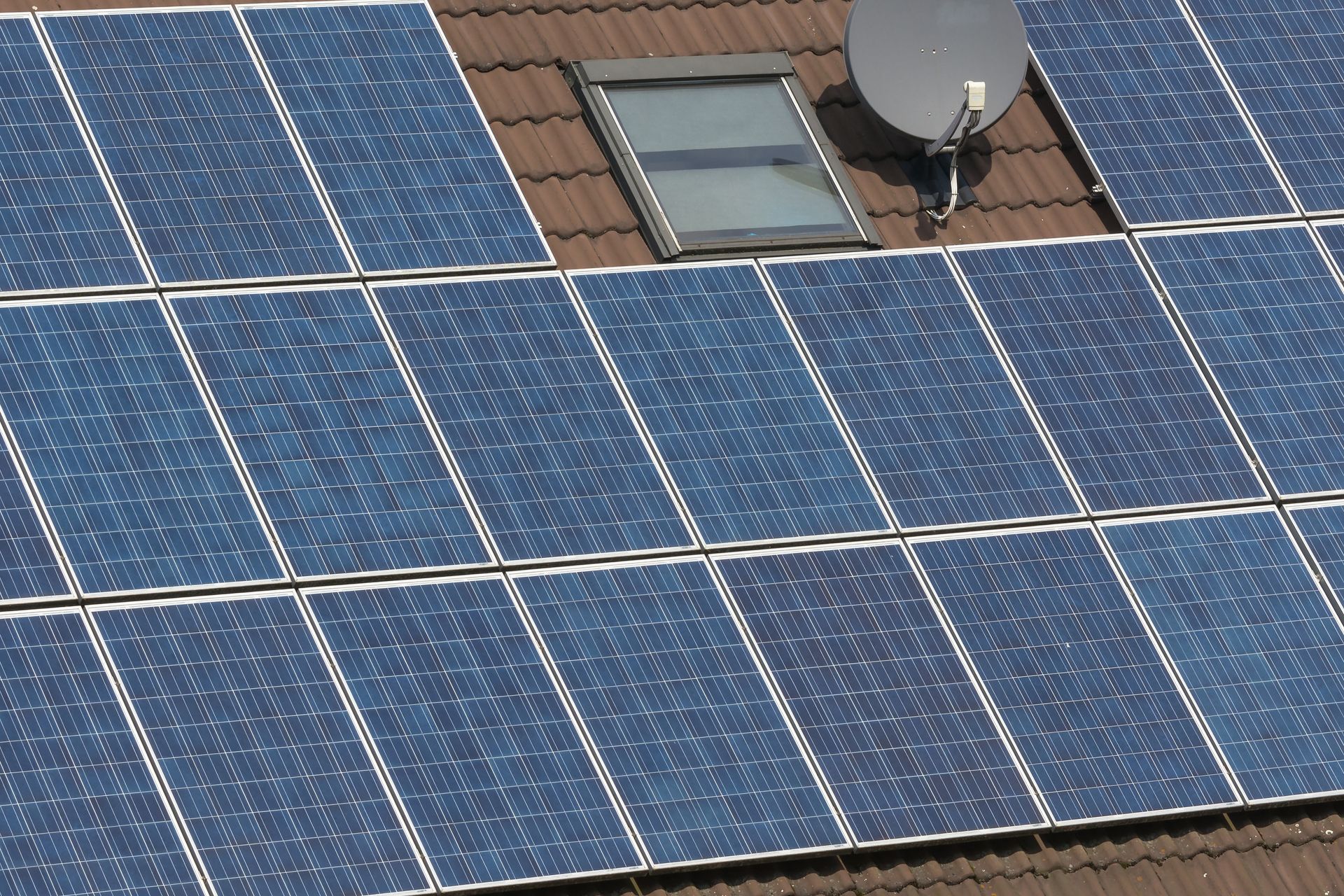 Solar panels on a brown tiled roof with a skylight and satellite dish.