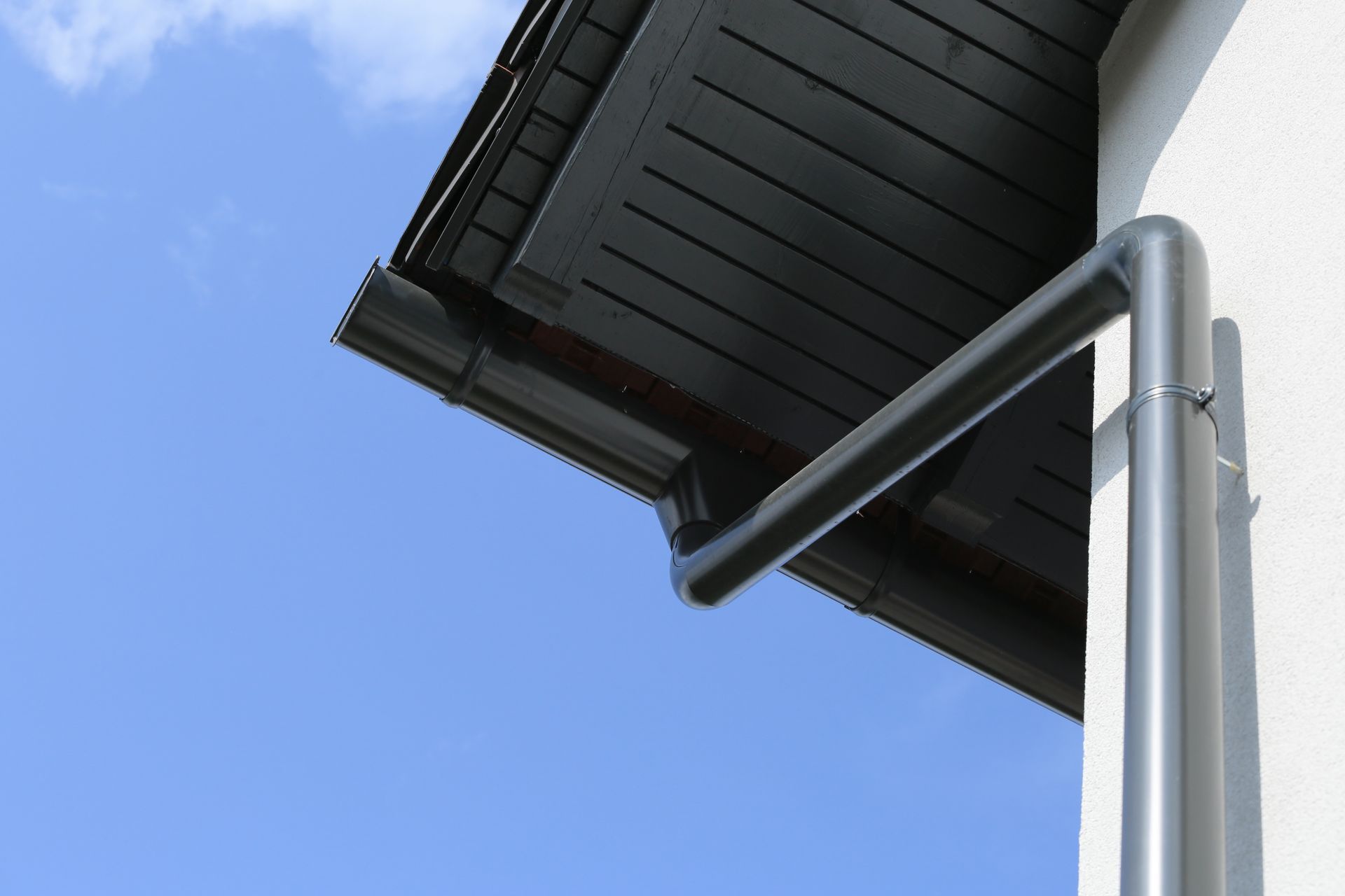 Gray rain gutter and downspout on a white building against a blue sky.