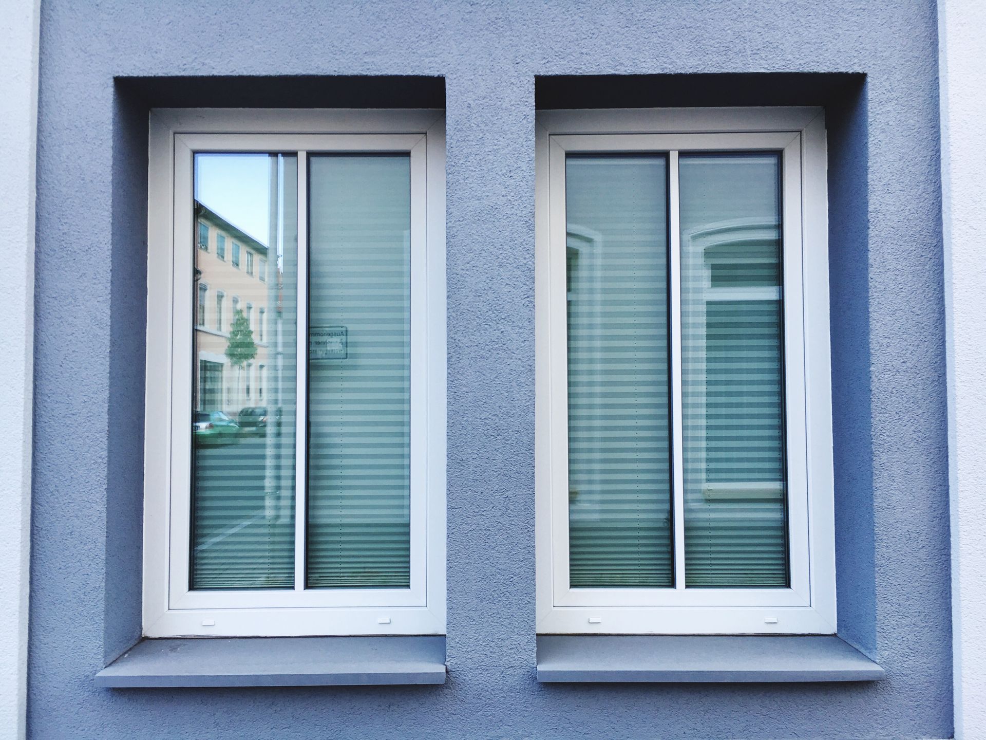 Two windows on a blue building with blinds on them