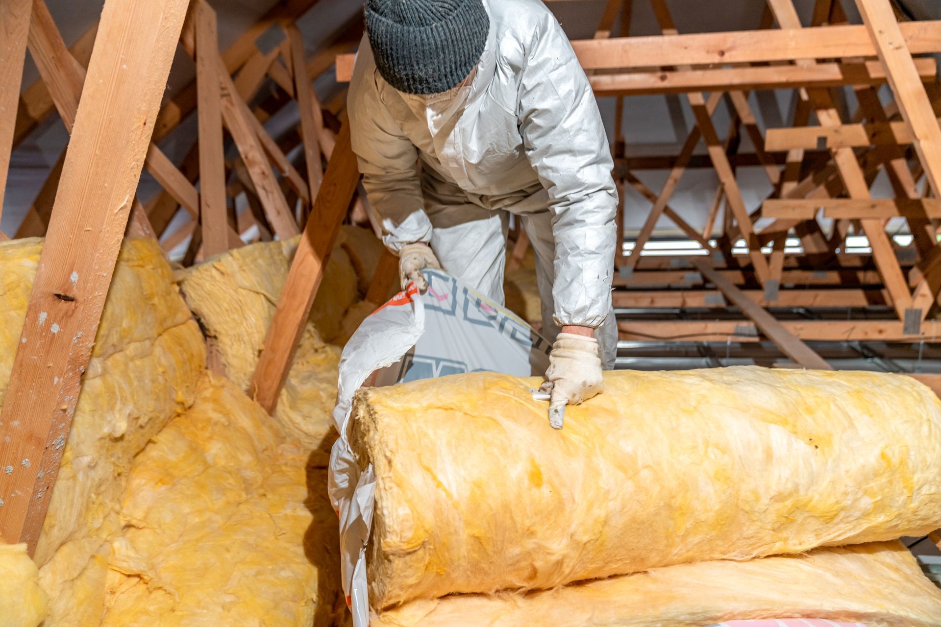 A man is cutting a roll of insulation in an attic.