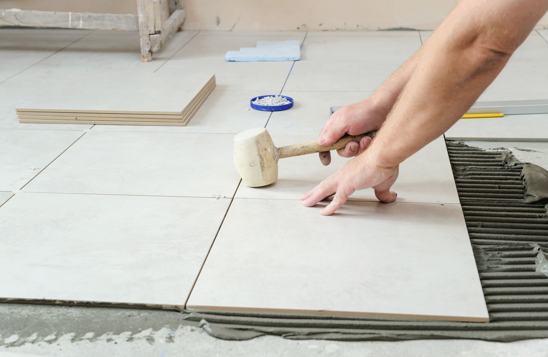A person is laying tiles on the floor with a hammer.