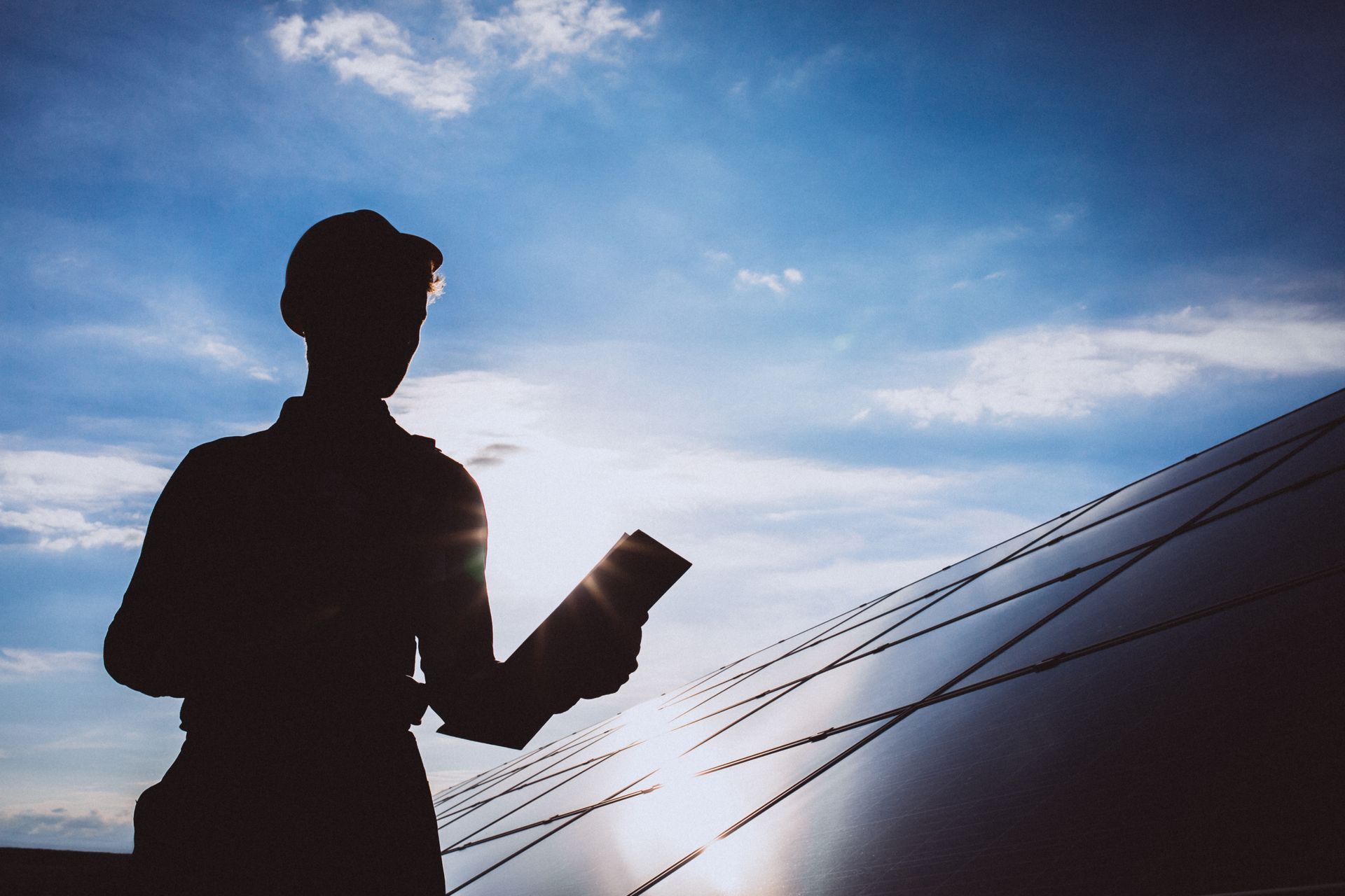 A silhouette of a man standing in front of a solar panel holding a clipboard.