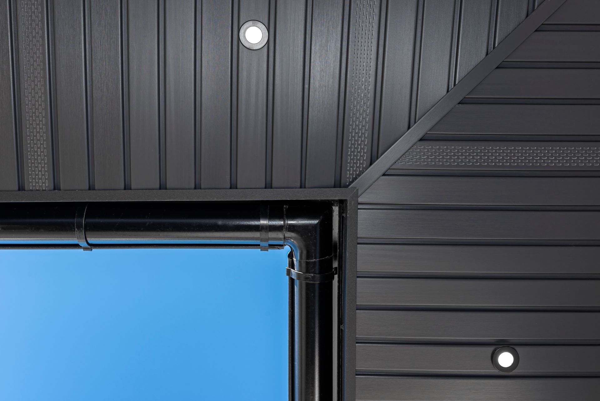 A close up of a black wall with a blue sky in the background.