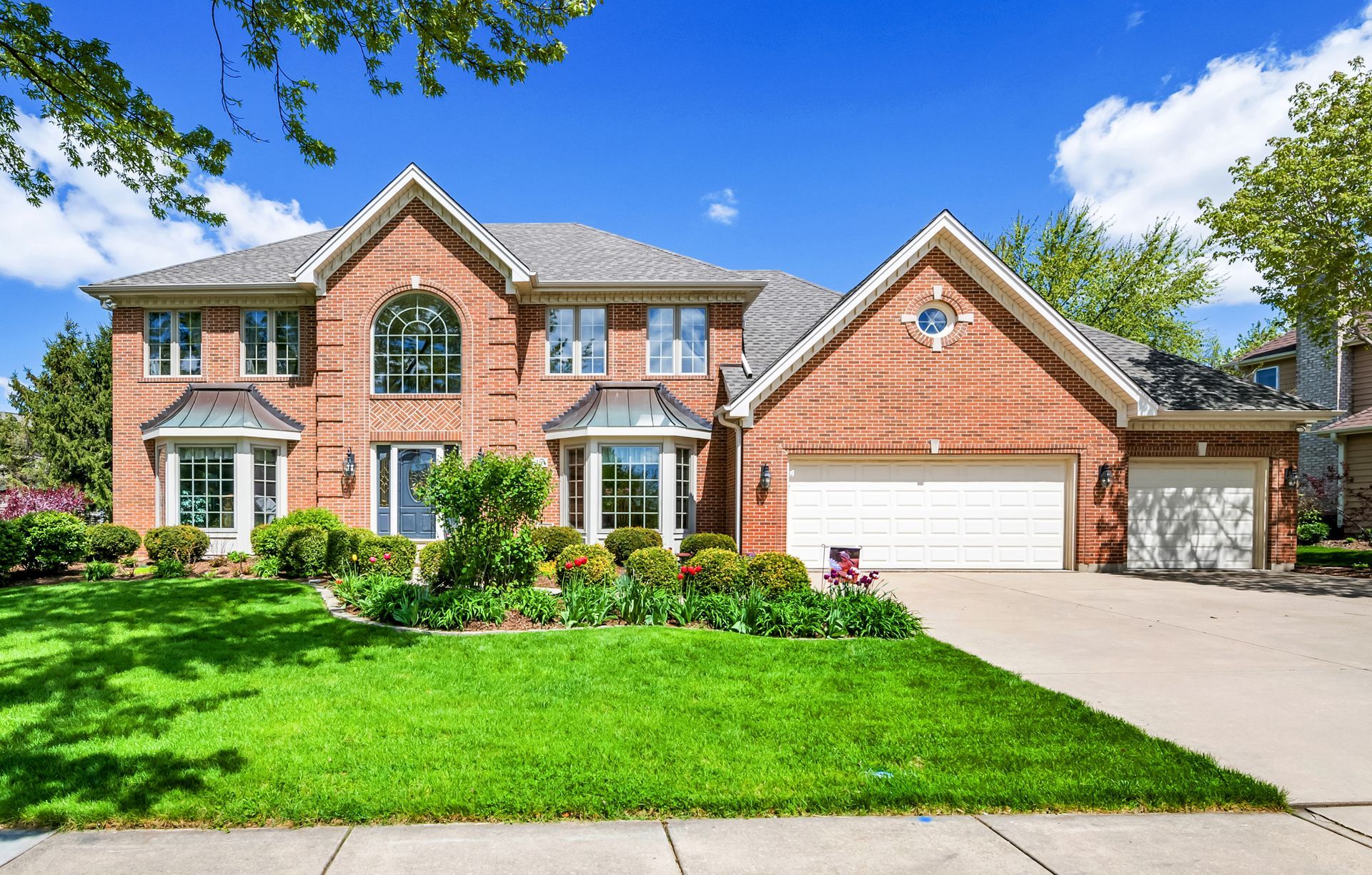 A large brick house with a white garage door and a lush green lawn.