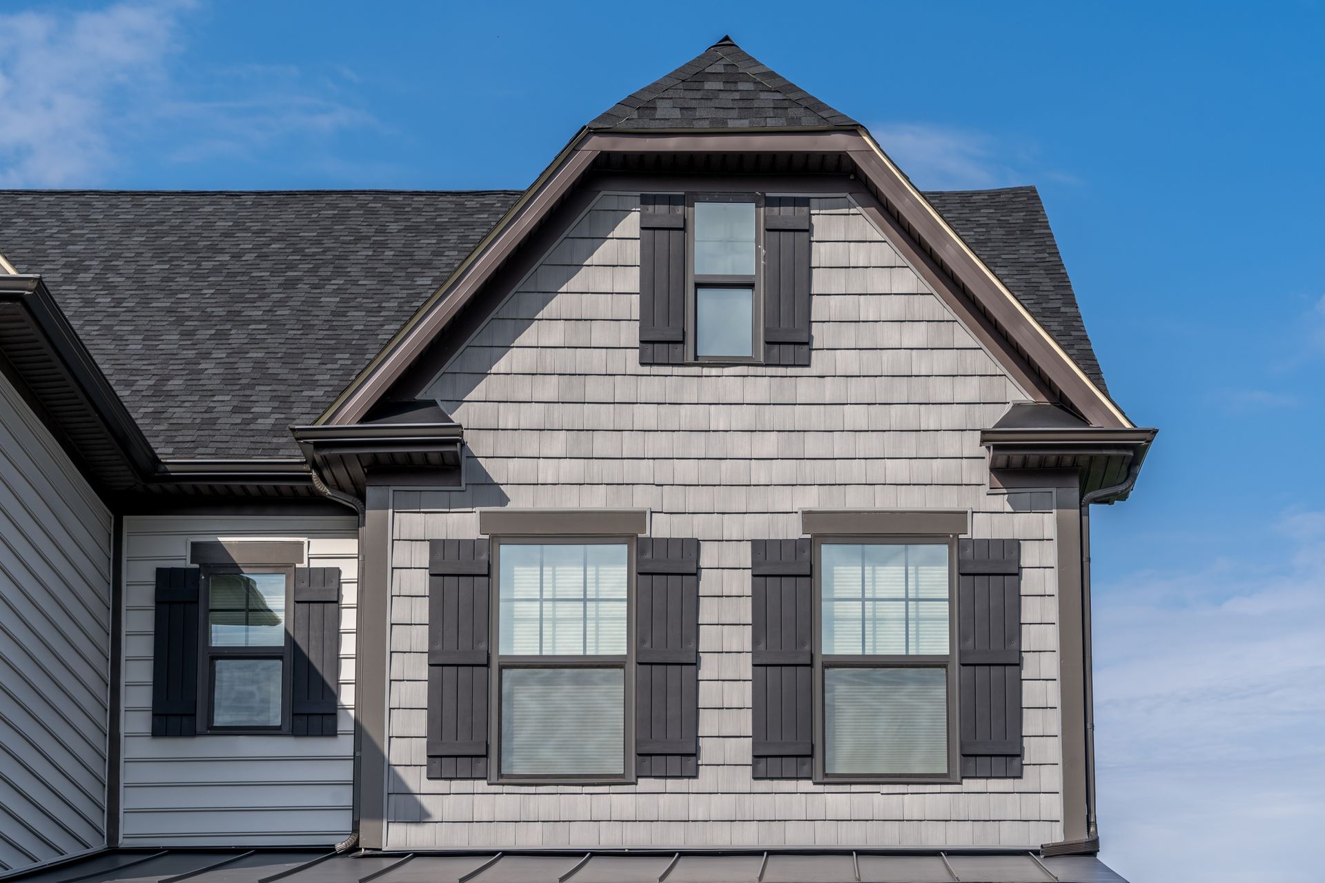 The front of a house with black shutters and a blue sky in the background.
