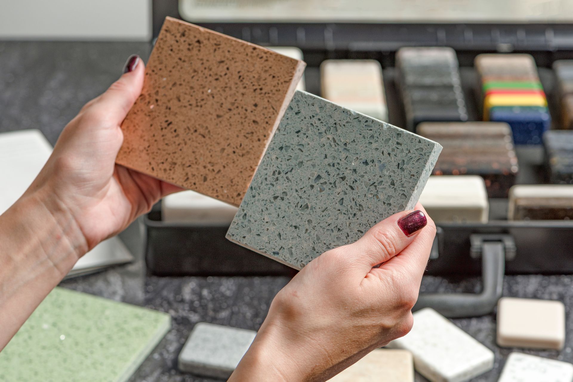 A woman is holding two tiles in her hands in front of a tray of tiles.