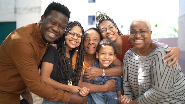 Group of smiling Black family members posing together outside.