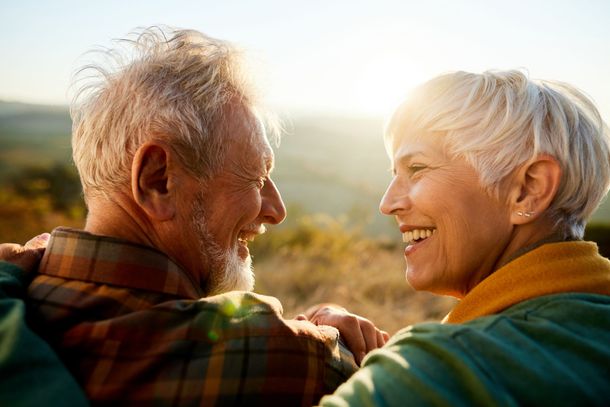 Smiling older couple looking at each other outdoors in a sunny setting. They are embracing, radiating happiness.