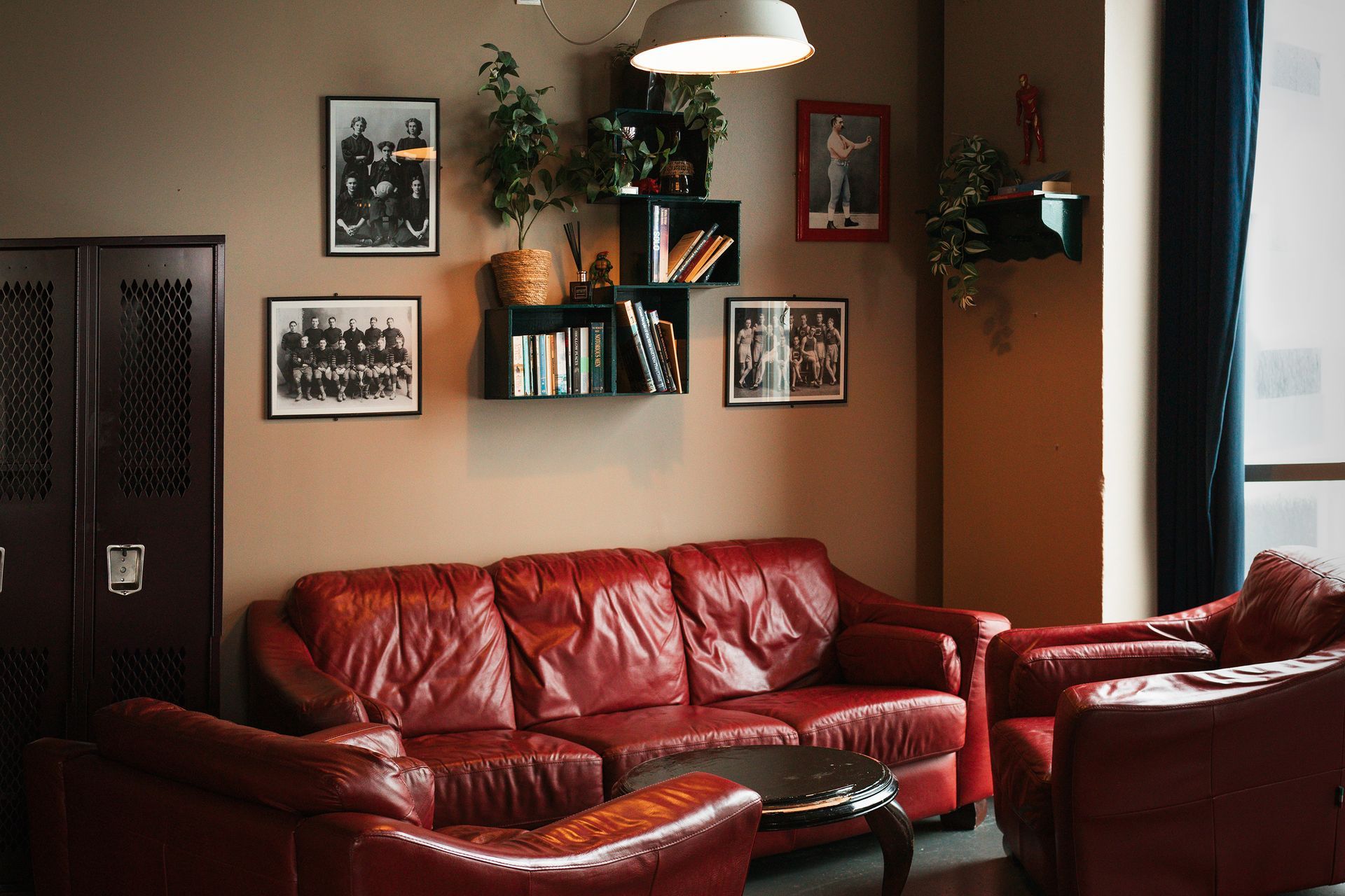 Red leather couches and armchairs in a living room, brown walls, framed photos, plants, and a dark cabinet.