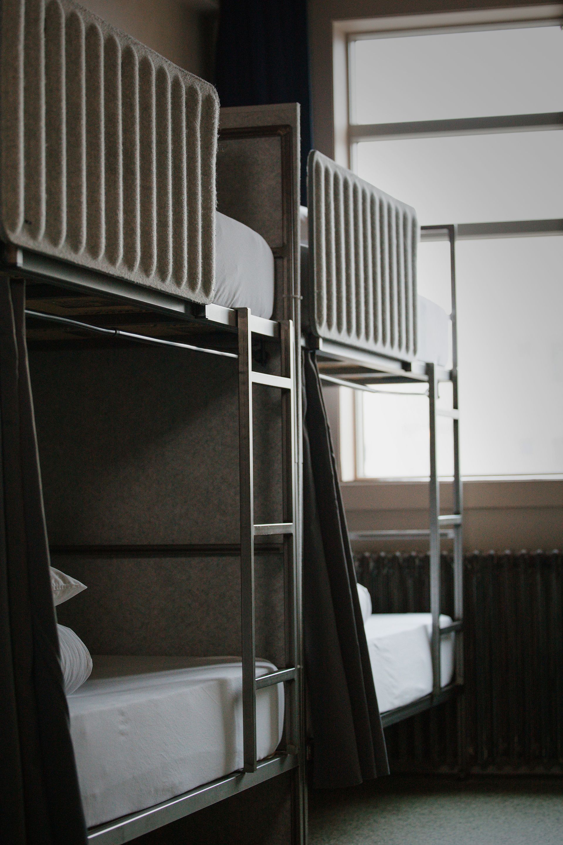 Two bunk beds in a room with a window, white sheets, and metal frames.