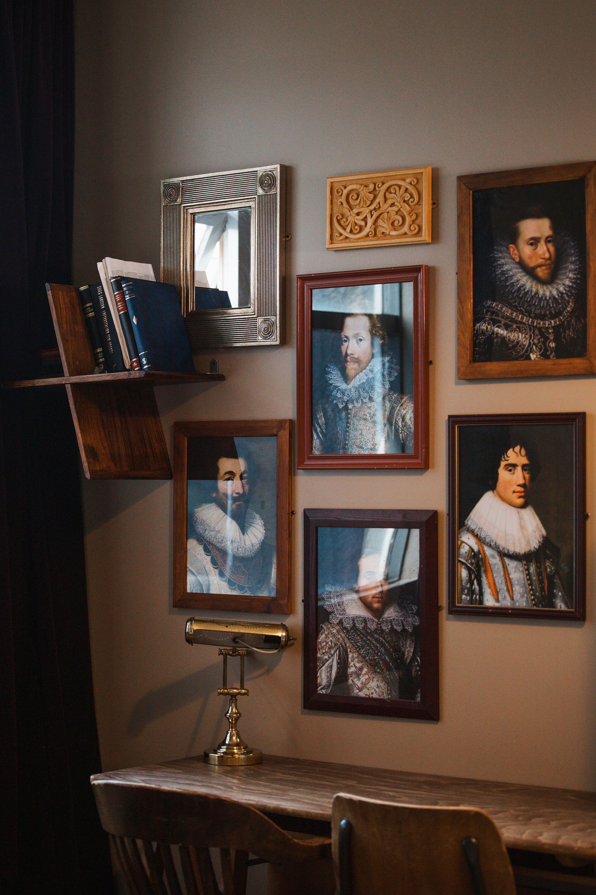 Desk with portraits and mirror on a wall, a bookshelf with books, and a lamp.