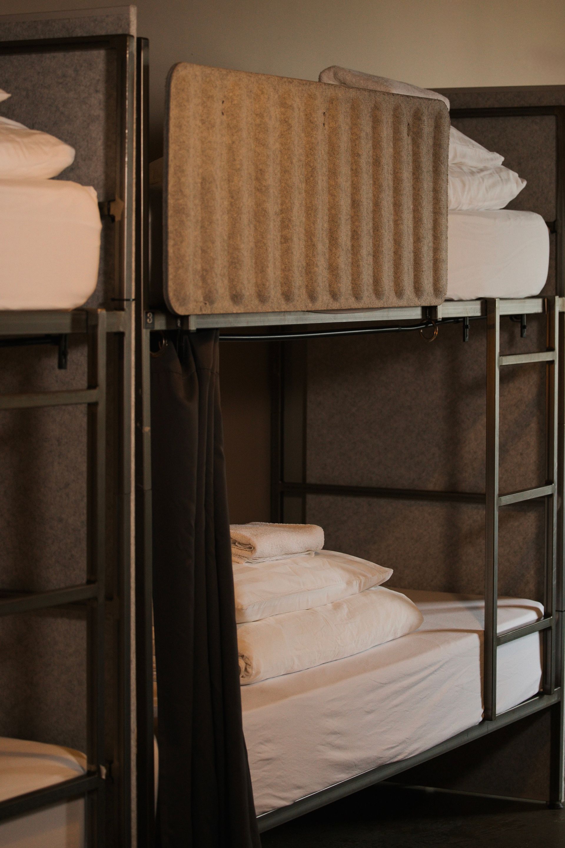 Metal bunk beds in a room, with white bedding and a privacy curtain.