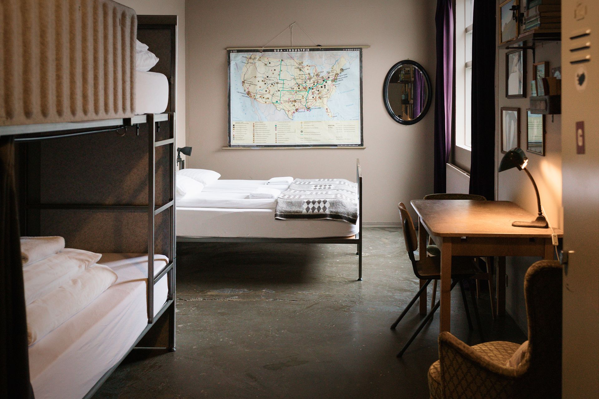 Hostel room with bunk beds, a single bed, desk, map, and dark purple curtains.