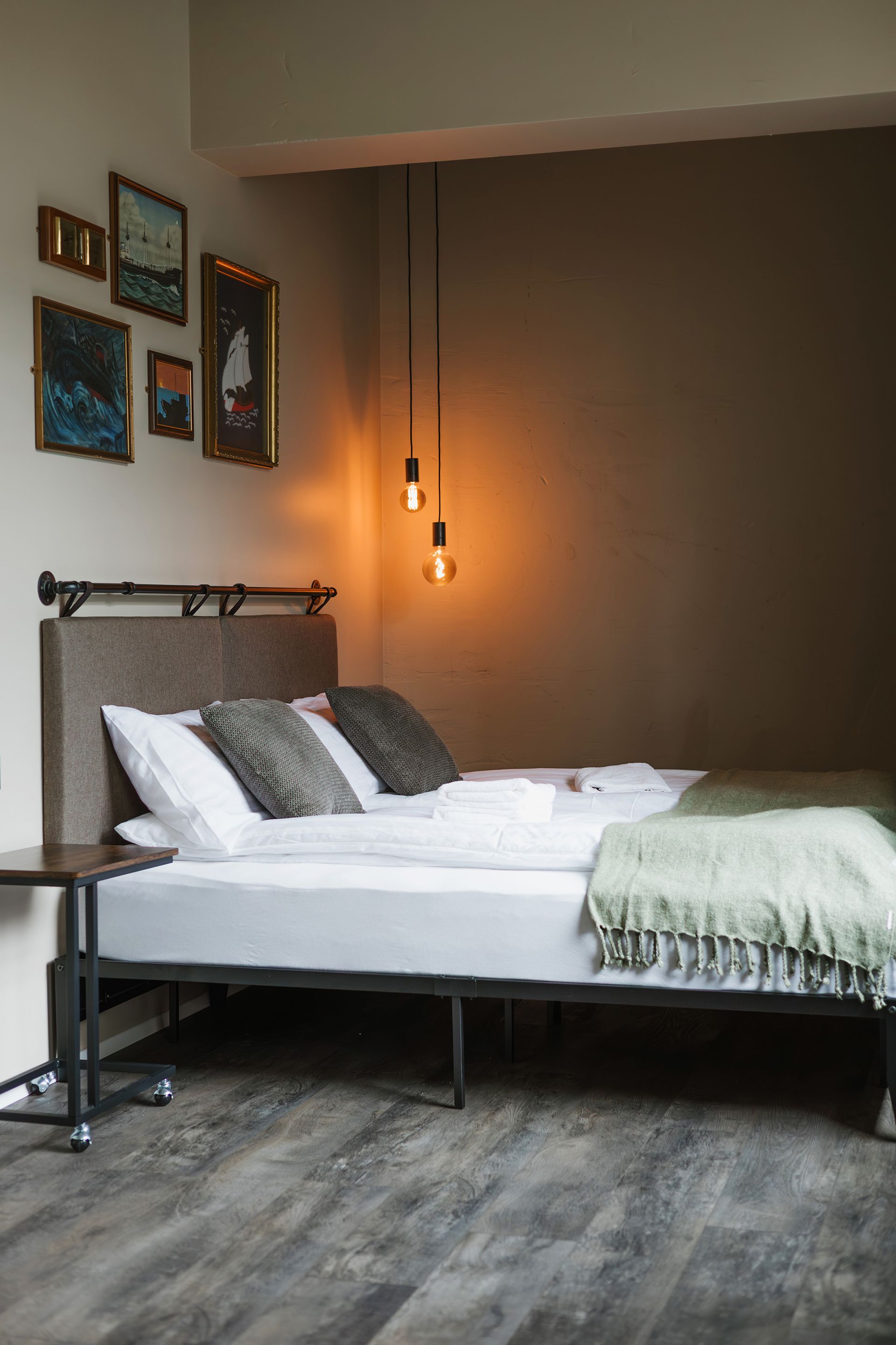 Bedroom with bed, art on wall, hanging lights, and dark wood flooring.