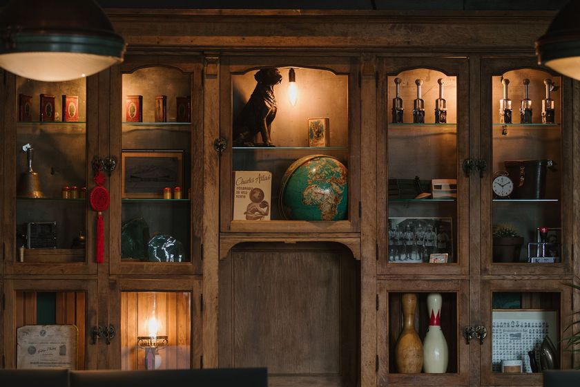 Wooden cabinet with various objects inside, including a dog statue, bowling pins, and a globe, illuminated by soft light.
