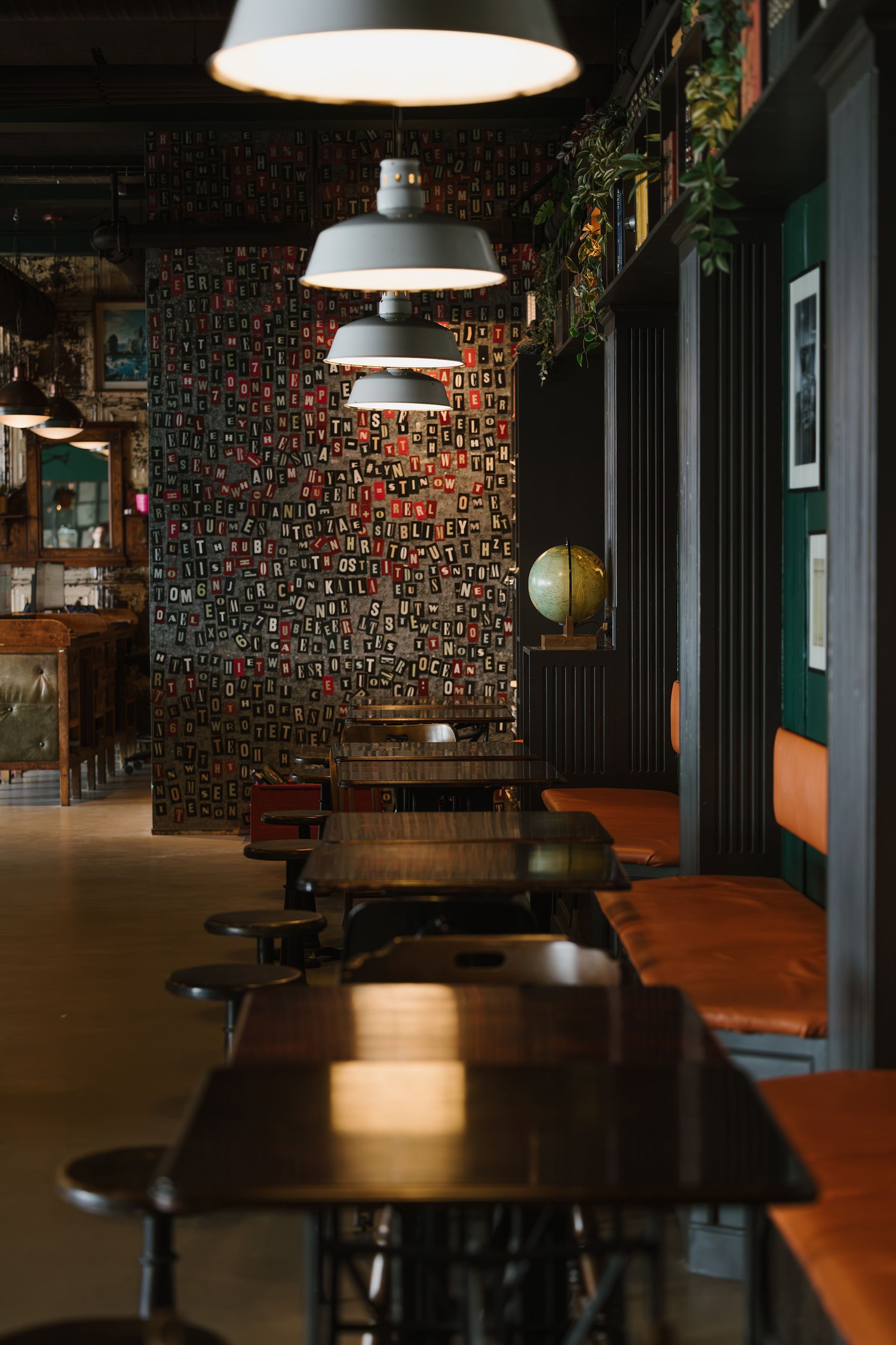 Dimly lit bar interior with tables, stools, pendant lights, and wall of small objects.