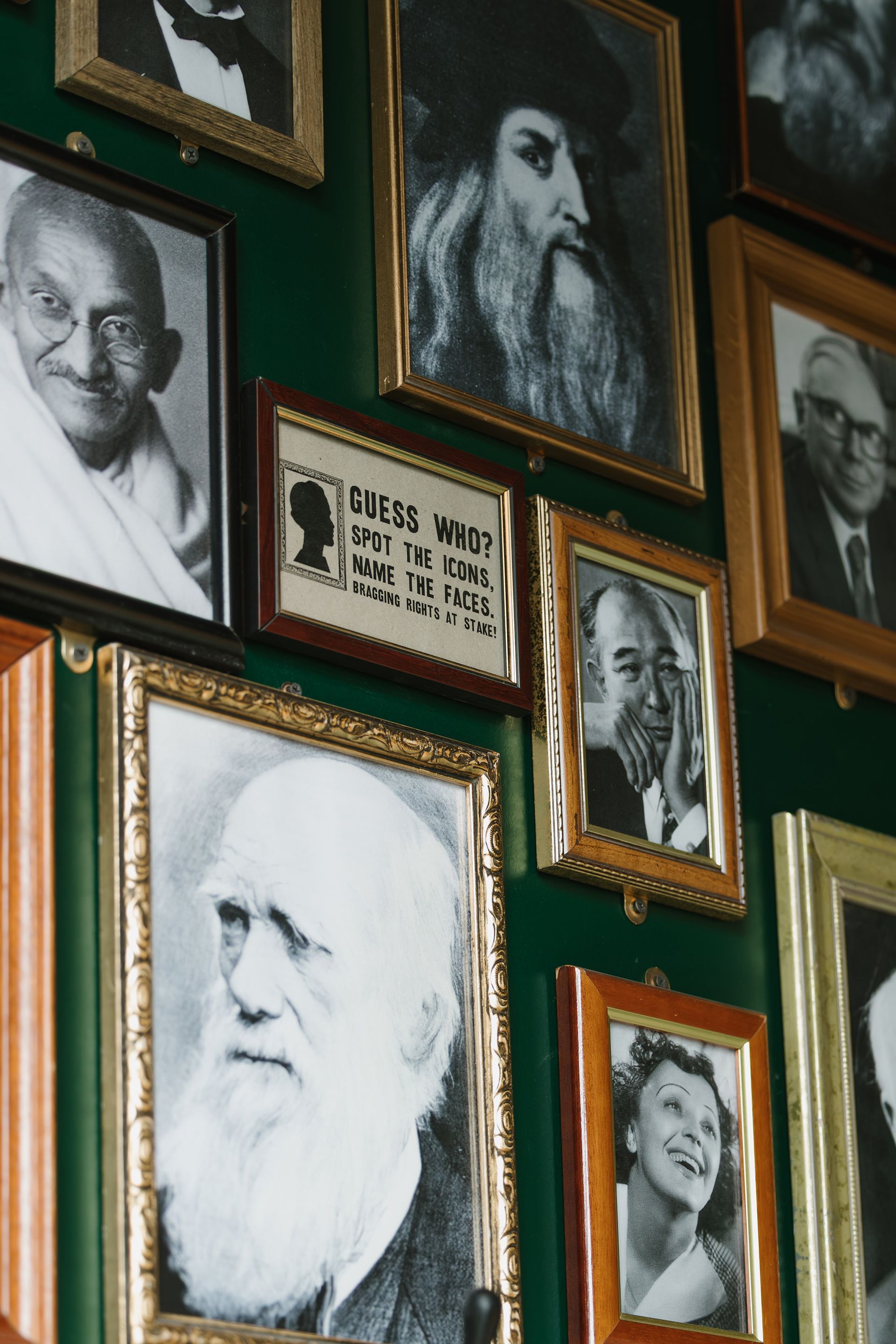 Framed portraits on a green wall, including Gandhi, Leonardo da Vinci, and Darwin.